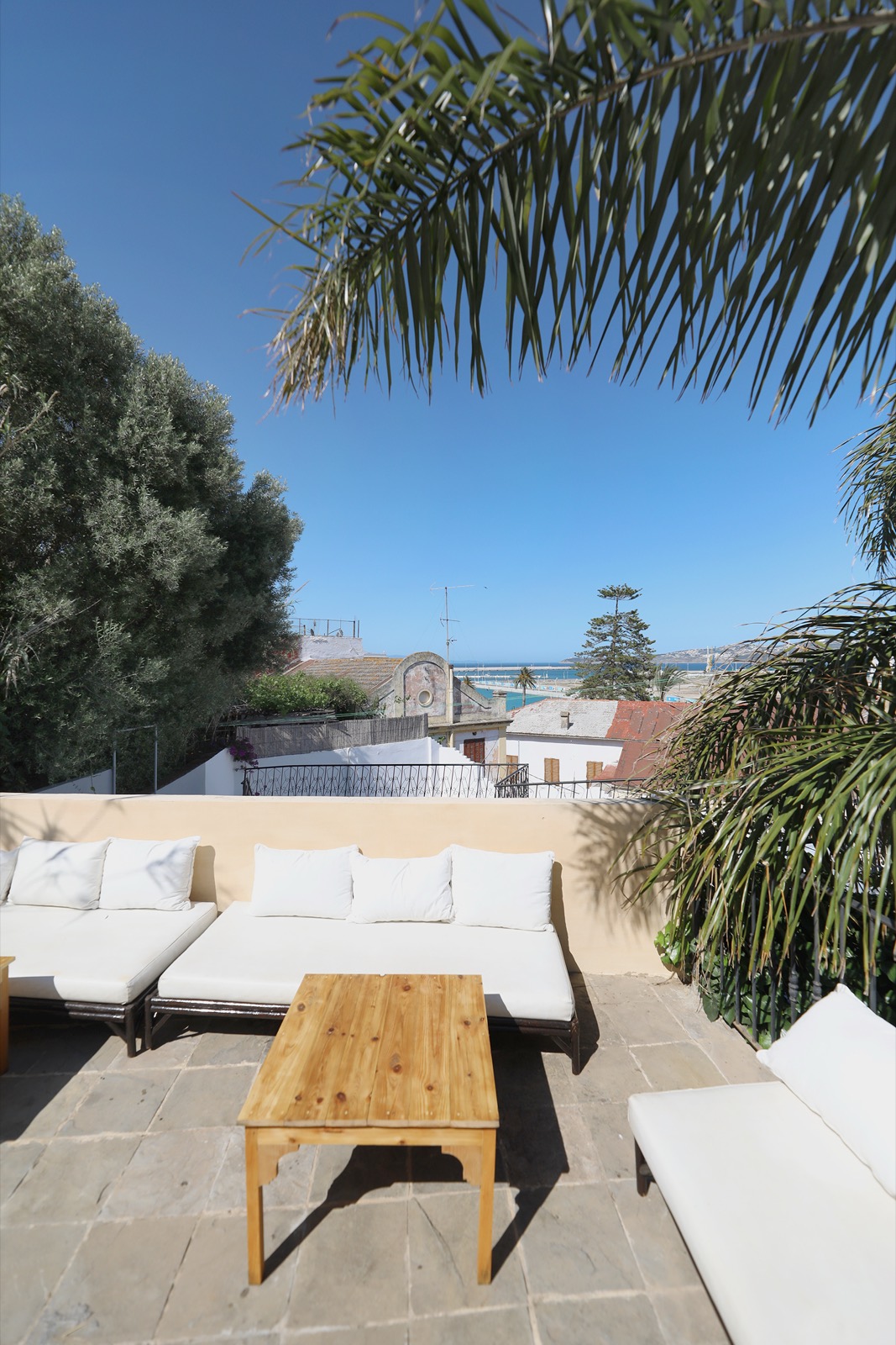 Un coin salon de terrasse &mdash; coussins blancs sous le palmier, la mer au loin