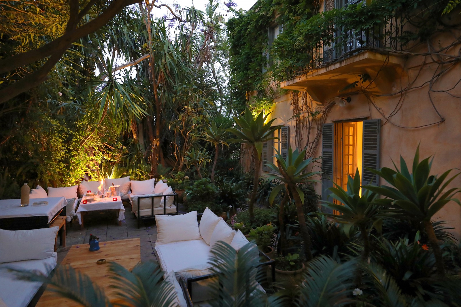 La table dressée au jardin à la nuit tombée, lanternes allumées parmi la végétation