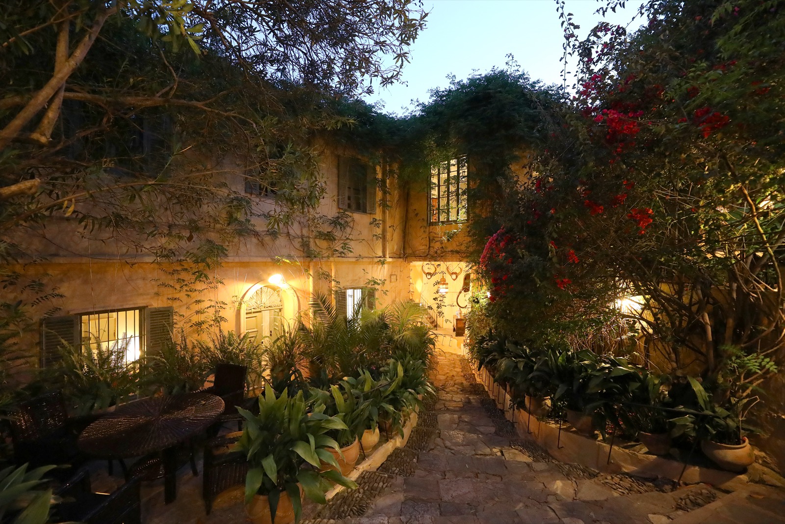 La villa au crépuscule, ses fenêtres éclairées derrière la végétation du jardin