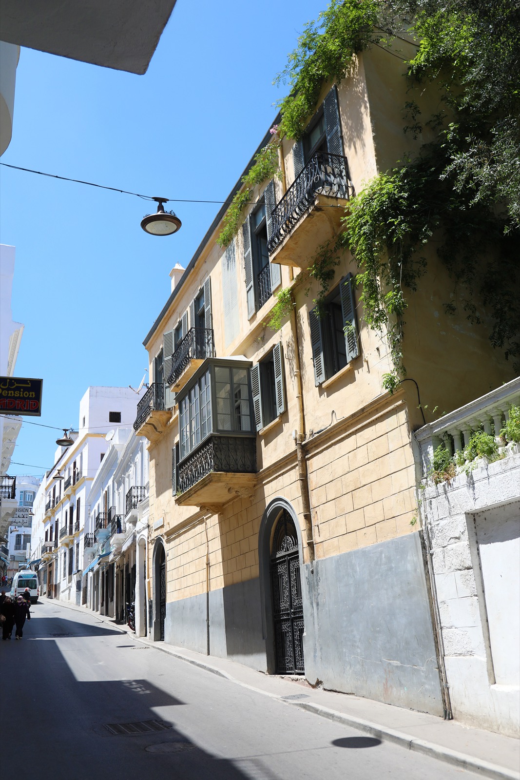 La façade discrète de Mimi Calpe sur la rue de la Plage, glycine débordant du mur et porte cintrée en fer forgé